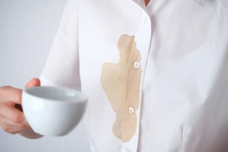 Filiżanka z kawą i plama z rozlanej kawy na białej tkaninie.